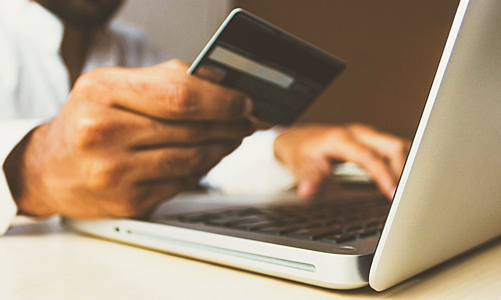 Close-up of hands holding a credit card and typing on a laptop keyboard, representing online purchasing or financial transactions.